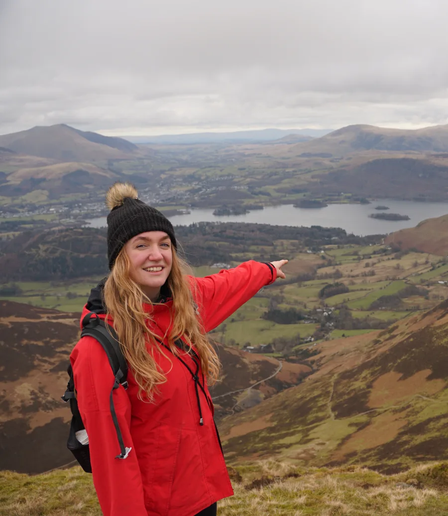 A hiker on a fell top pointing towards the download button